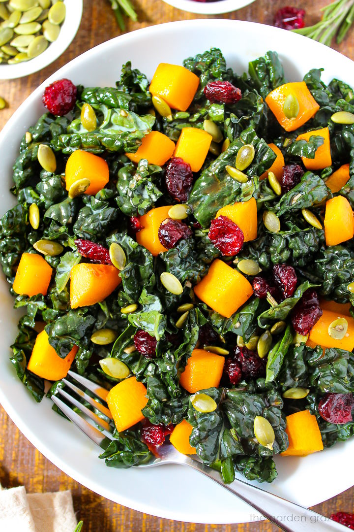 A bowl of butternut squash and kale salad with rosemary balsamic dressing on a wooden table