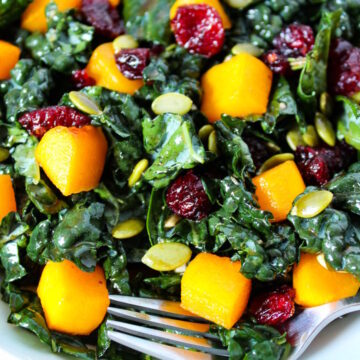 Close up view of butternut squash kale salad in a white bowl with serving fork