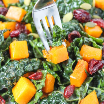 Close up view of a fork picking up butternut squash kale salad from a white plate