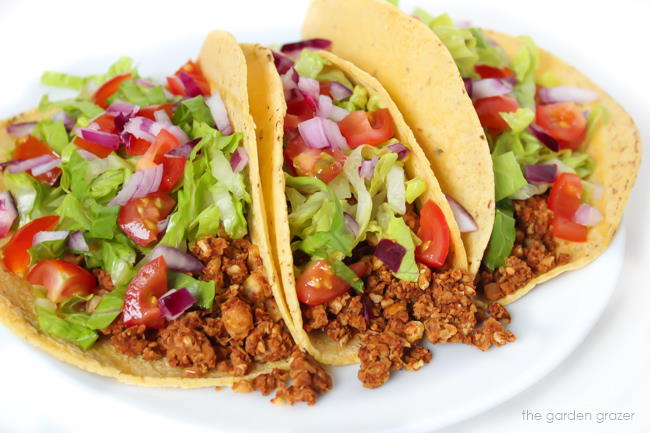 Plate of vegan tacos topped with romaine, tomato, and red onion