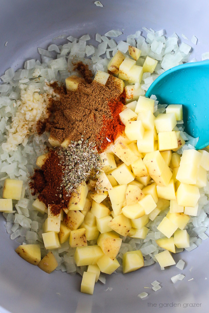 Overhead view of onion, potato, garlic, and seasonings cooking in a large stockpot