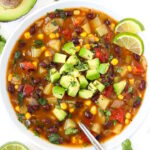 Southwest black bean soup in a white bowl garnished with avocado, cilantro, and lime slices