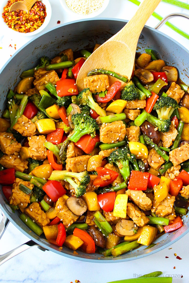 Overhead view of teriyaki vegetable stir fry cooking in a large skillet with spoon