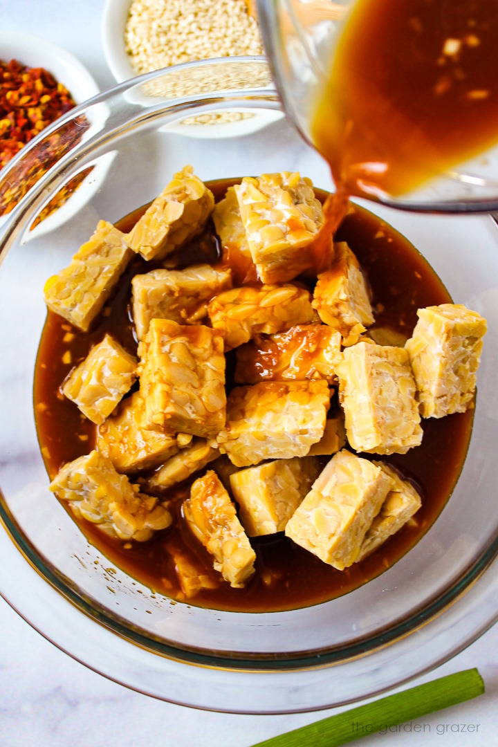 Chopped tempeh chunks being marinated in homemade teriyaki sauce in a glass bowl