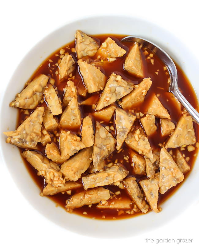 Triangles of tempeh marinating in teriyaki sauce in a bowl