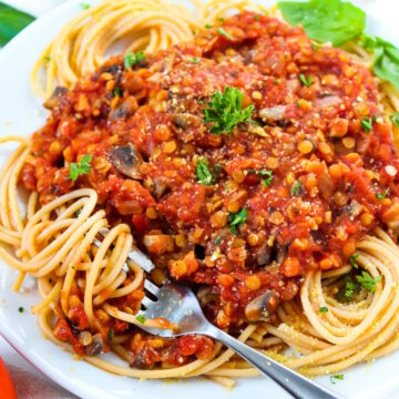 Close-up view of vegan lentil Bolognese sauce served over spaghetti noodles on a white plate with fresh herbs