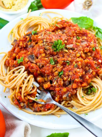 Close-up view of vegan lentil Bolognese sauce served over spaghetti noodles on a white plate with fresh herbs