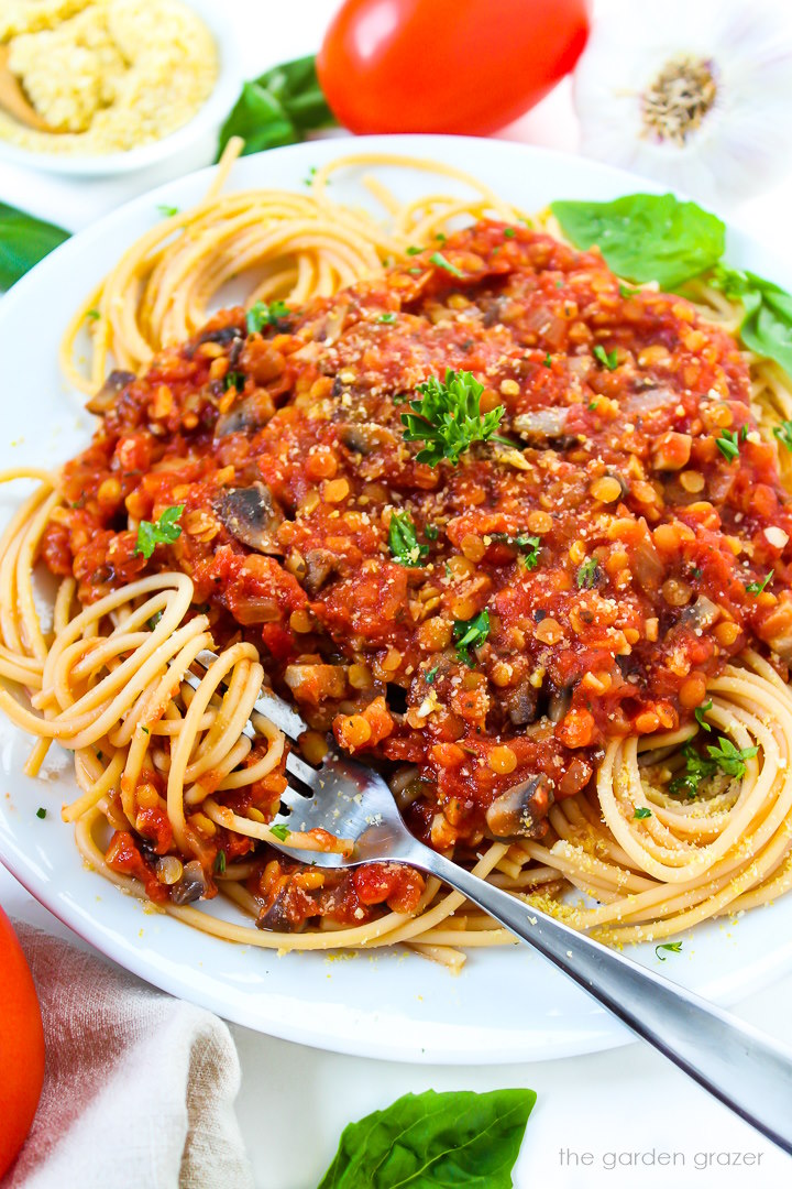 Close-up view of vegan lentil Bolognese sauce served over spaghetti noodles on a white plate with fresh herbs