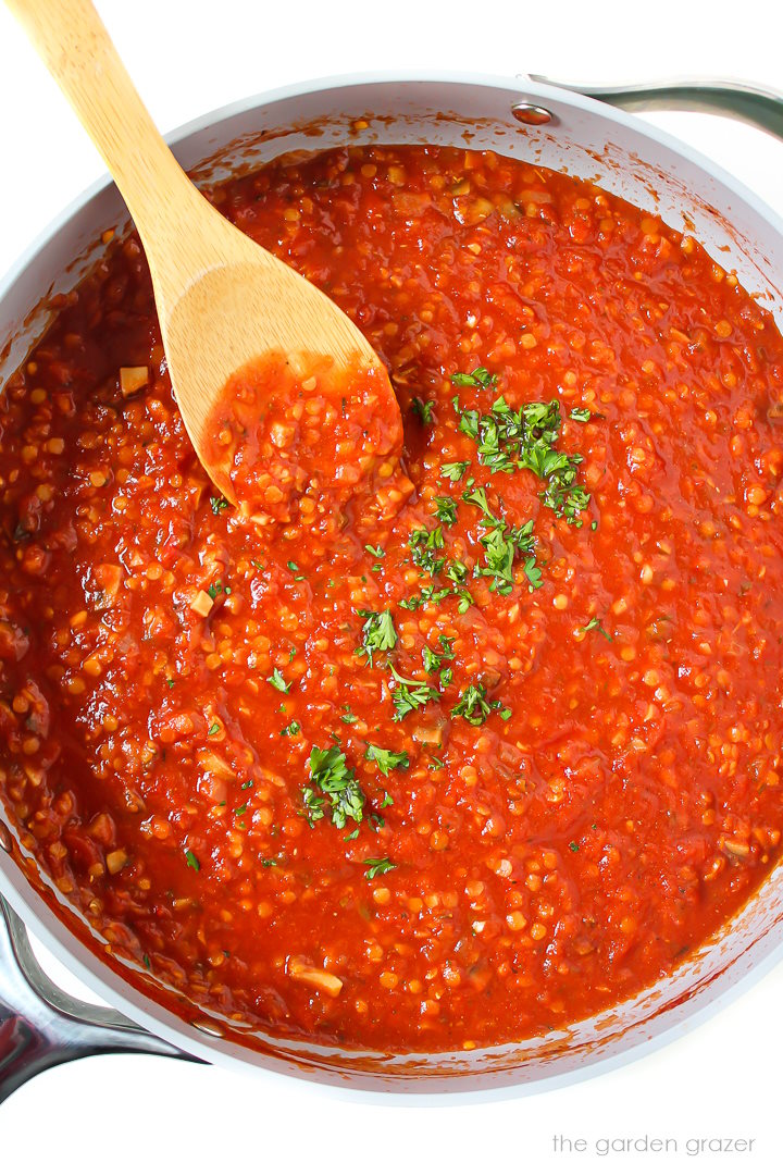 Vegan lentil Bolognese sauce cooking in a large skillet with bamboo stirring spoon