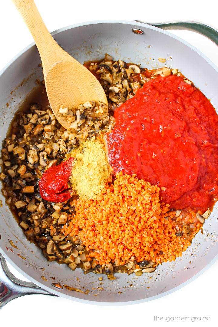 Overhead view of sauce preparation in a large skillet with wooden stirring spoon