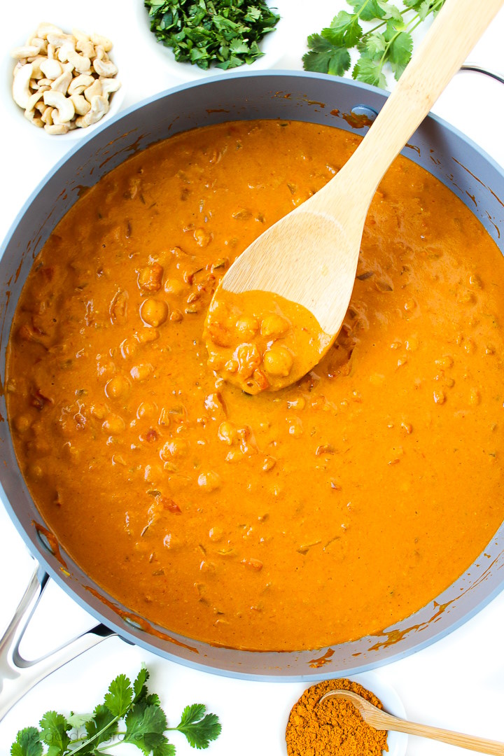 Butter chickpeas cooking in a large skillet with wooden stirring spoon