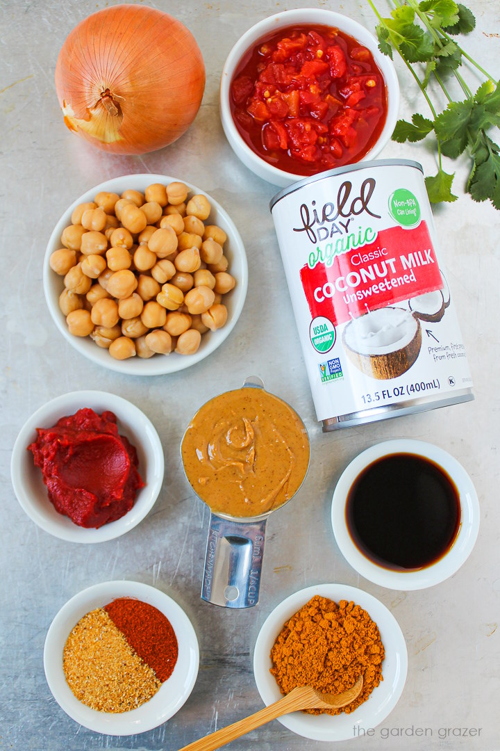 Canned coconut milk, diced tomatoes, peanut butter, tomato paste, onion, and spice ingredients laid out on a metal tray
