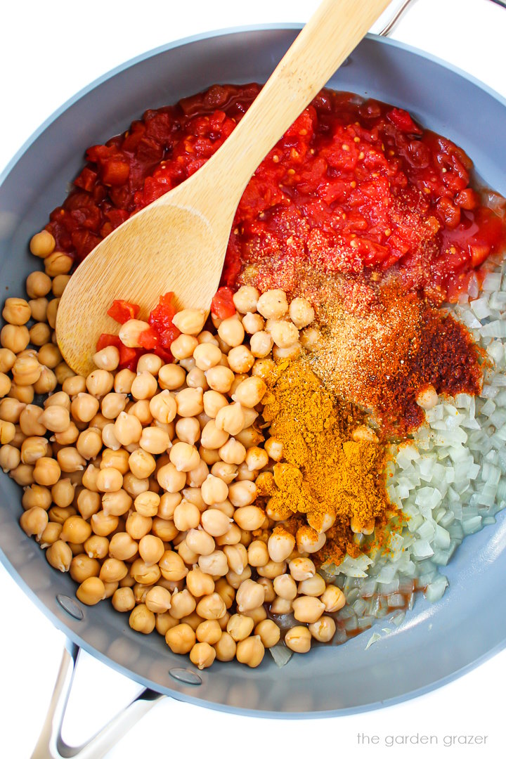 Overhead view of preparing chickpeas, tomatoes, and spices in a large skillet