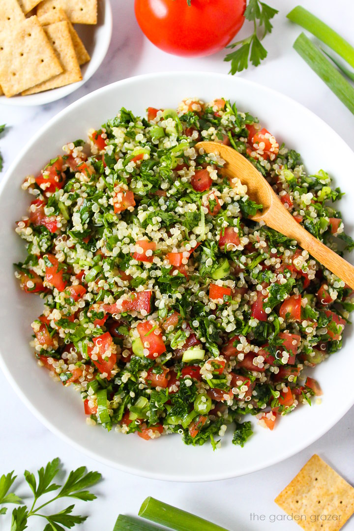 Overhead view of quinoa tabbouleh served in a white bowl with side of crackers