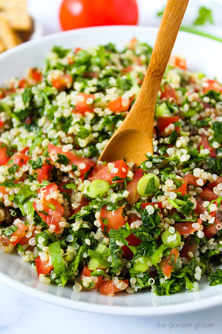 Close up view of quinoa tabbouleh in a white serving bowl with wooden spoon