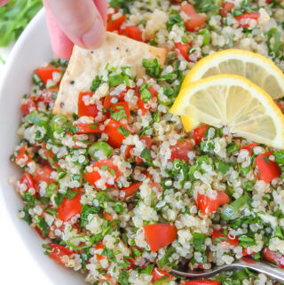 Cracker dipping into bowl of quinoa tabbouleh salad