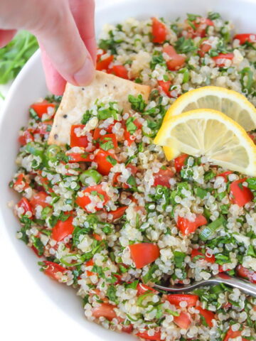 Cracker dipping into bowl of quinoa tabbouleh salad