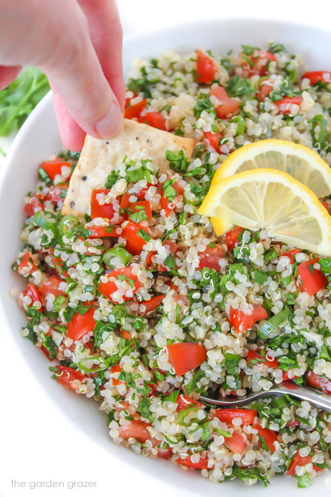 Cracker dipping into bowl of gluten-free quinoa tabbouleh salad