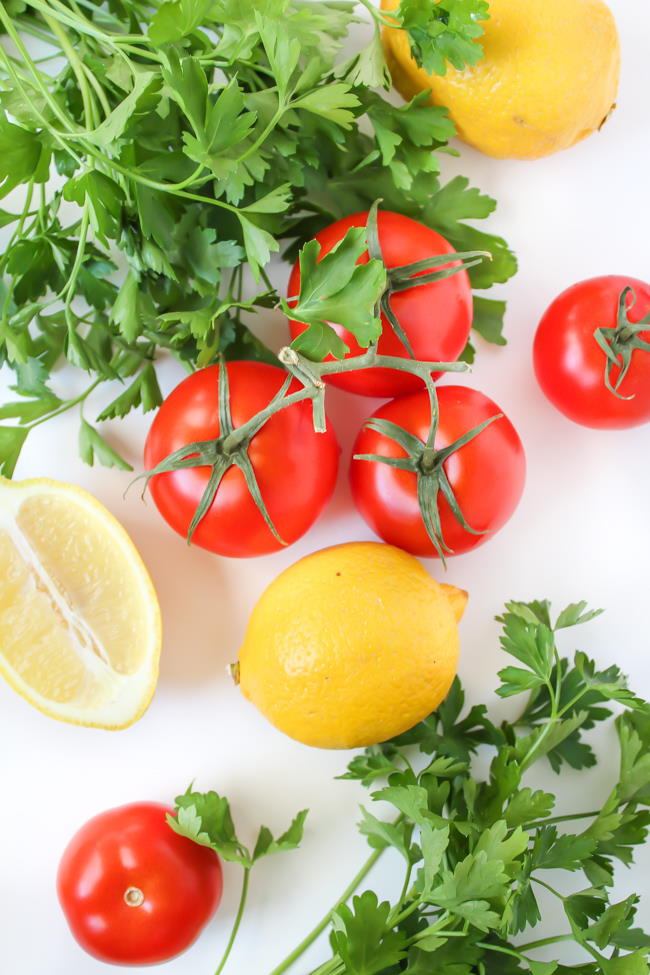 Fresh tomatoes, parsley, and lemons on a cutting board
