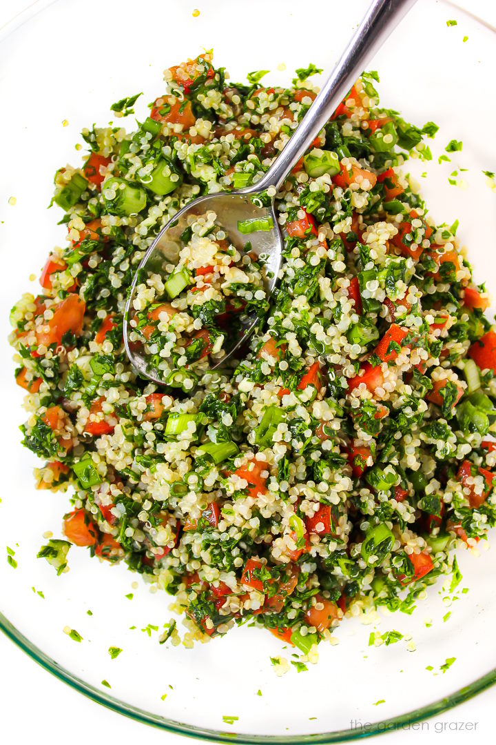 Quinoa tabbouleh mixed together in a large glass bowl with metal spoon
