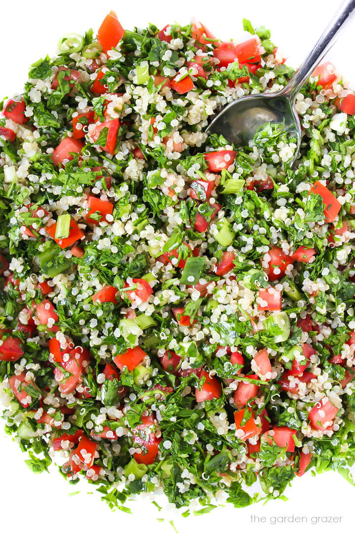 Fresh quinoa tabbouleh tossed together in a glass bowl with spoon