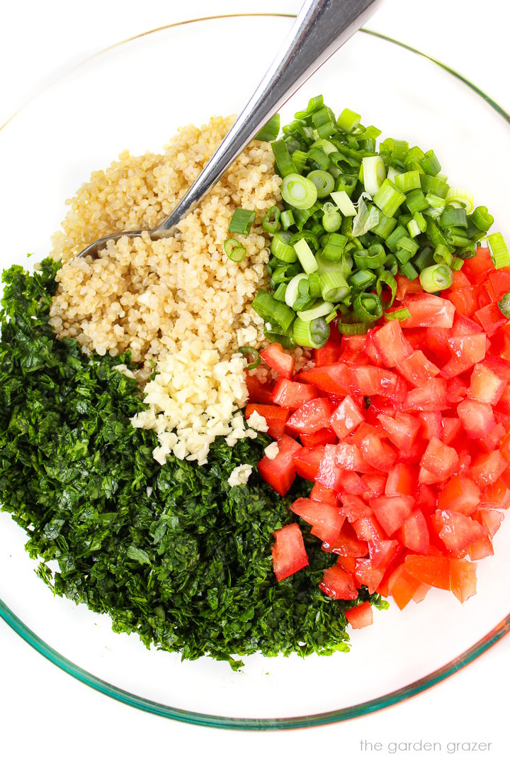 Overhead view of tabbouleh salad preparation in a large glass bowl before mixing together