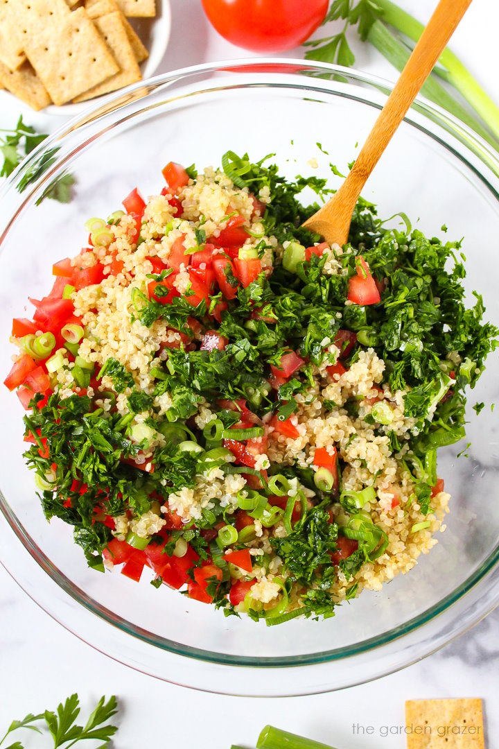 Preparing tomato, parsley, green onion, and garlic ingredients in a large glass bowl before mixing together