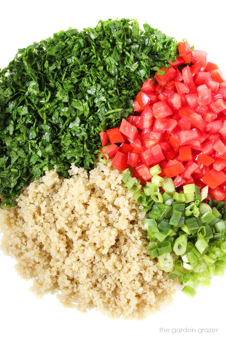 Cooked quinoa, green onion, chopped parsley, and diced tomato in a glass bowl