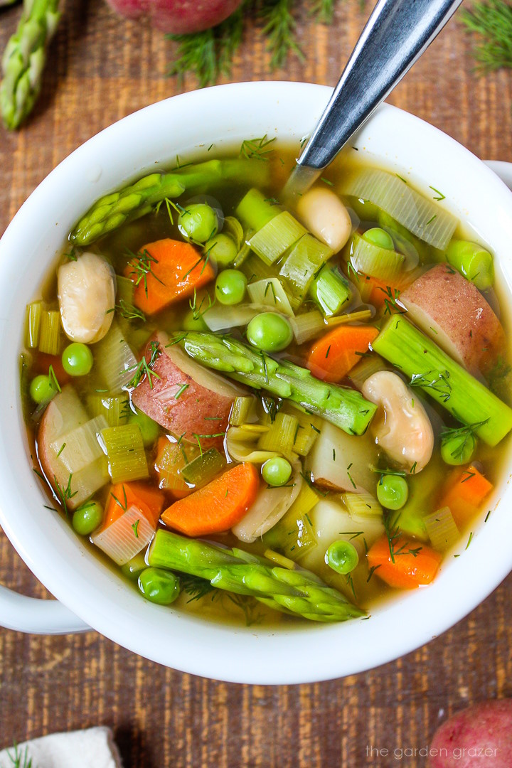 Close up view of vegan spring minestrone soup in a white serving bowl with spoon