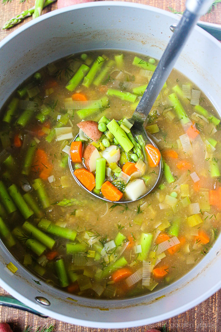 A ladle lifting up spring minestrone soup from a large cooking pot