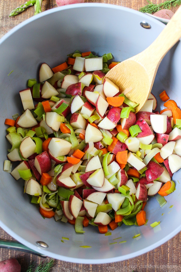Overhead view of preparing potato, leek, and carrot ingredients in a large pot with wooden stirring spoon
