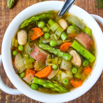 Spring minestrone soup with fresh dill in a white bowl with serving spoon