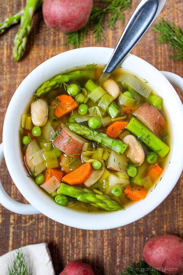 Spring minestrone soup with fresh dill in a white bowl with serving spoon