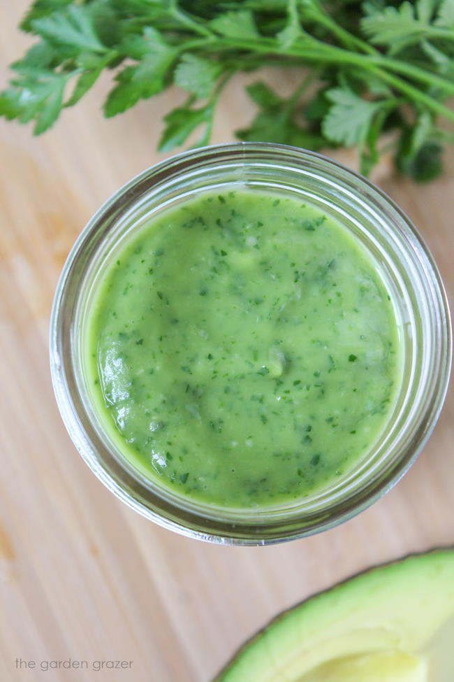 Jar of vegan avocado herb dressing with fresh basil and parsley