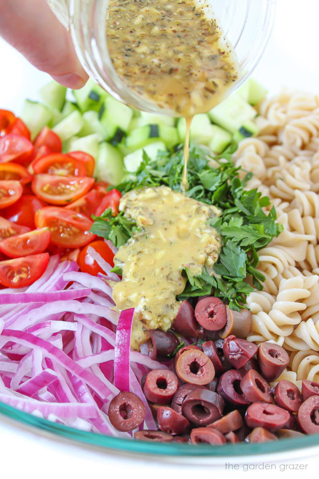 Chopped fresh ingredients in a bowl with dressing being poured on top