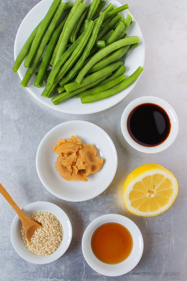Fresh green beans, white miso paste, tamari, lemon, and sesame seed ingredients laid out on a metal tray