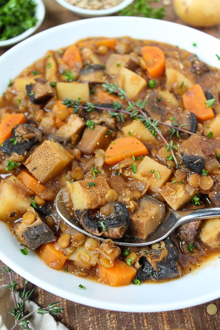 Close up view of Portobello mushroom stew in a white bowl with serving spoon