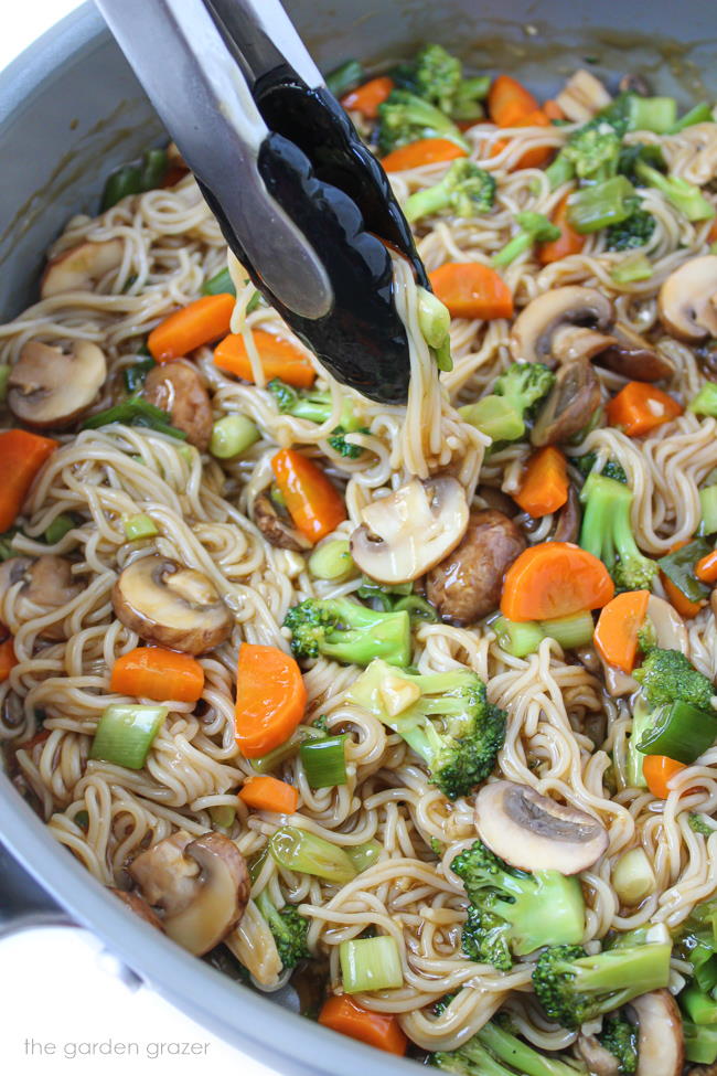 Cooking and preparing teriyaki noodles in a skillet with tongs