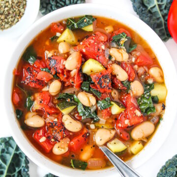White bean tomato soup with kale in a white bowl with spoon