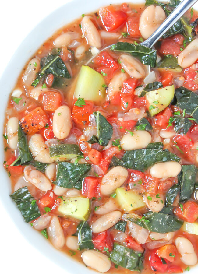 Vegan white bean soup with tomatoes and kale in a bowl with spoon