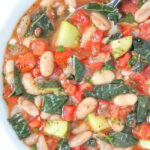 Vegan white bean soup with tomatoes and kale in a bowl with spoon