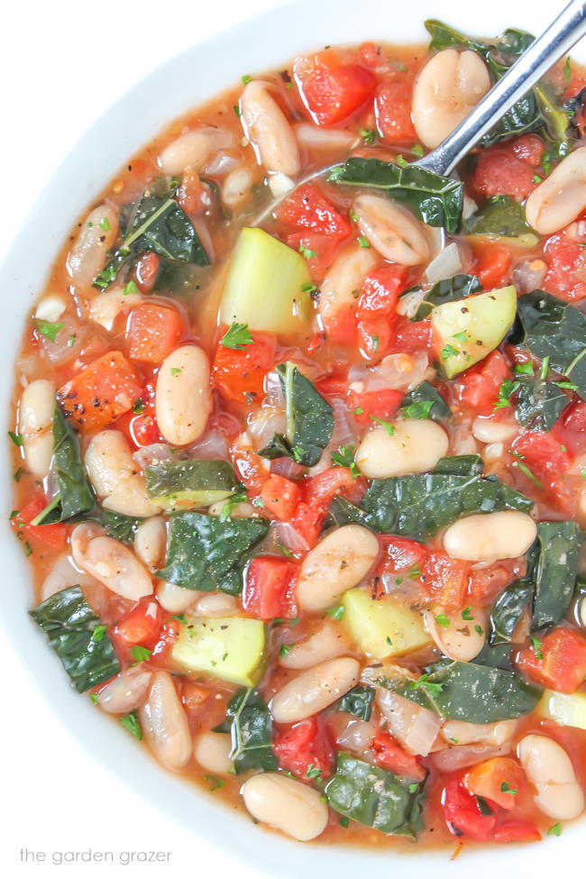 Vegan white bean soup with tomatoes and kale in a bowl with spoon