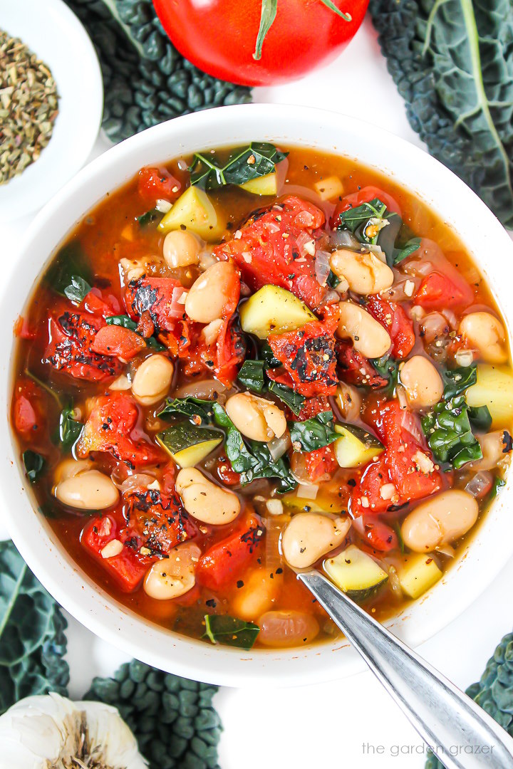 Overhead view of vegan white bean tomato soup with zucchini and kale in a white bowl