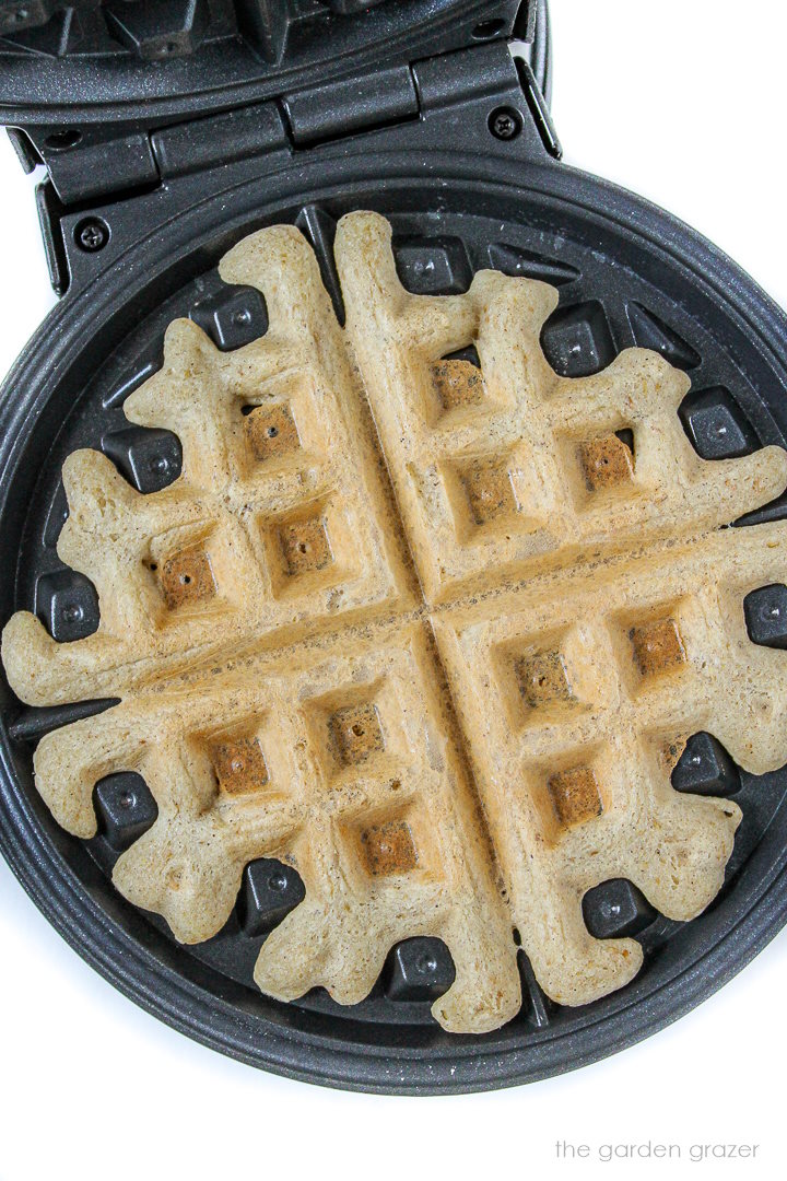 Overhead view of vegan gluten-free waffle cooking in a hot waffle iron with lid open