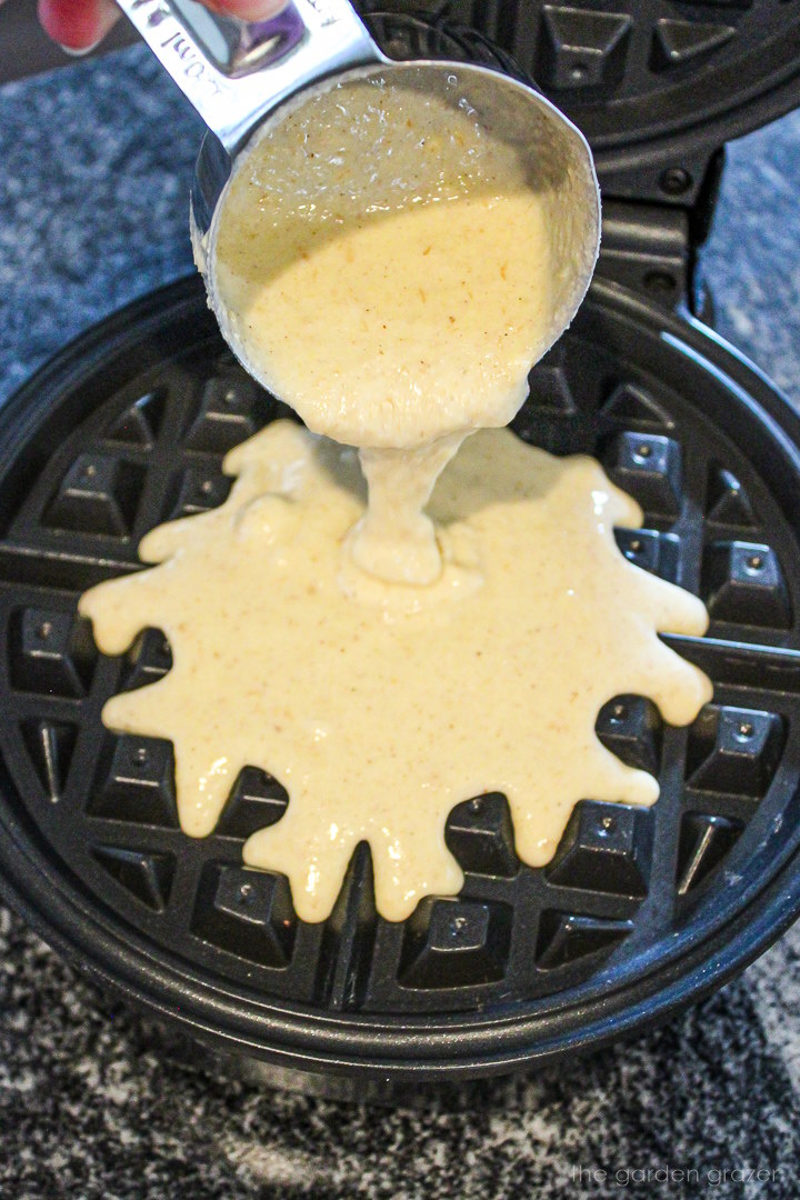 Pouring pancake batter from a measuring cup onto a hot waffle iron