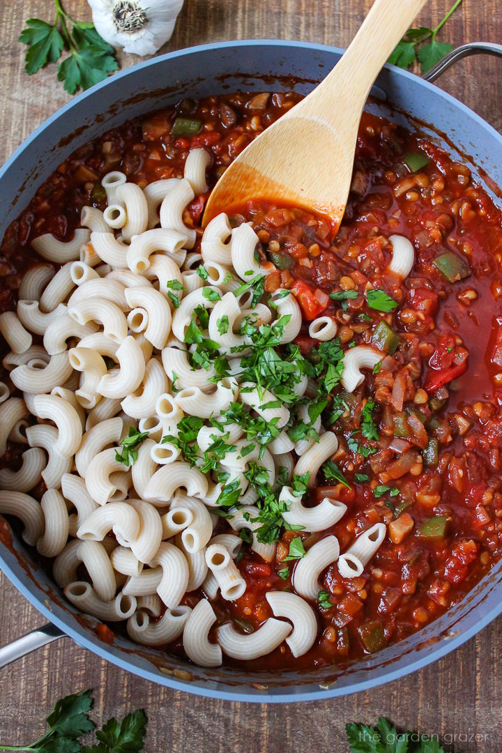 Overhead view of preparing lentil vegan goulash in a large skillet with wooden stirring spoon