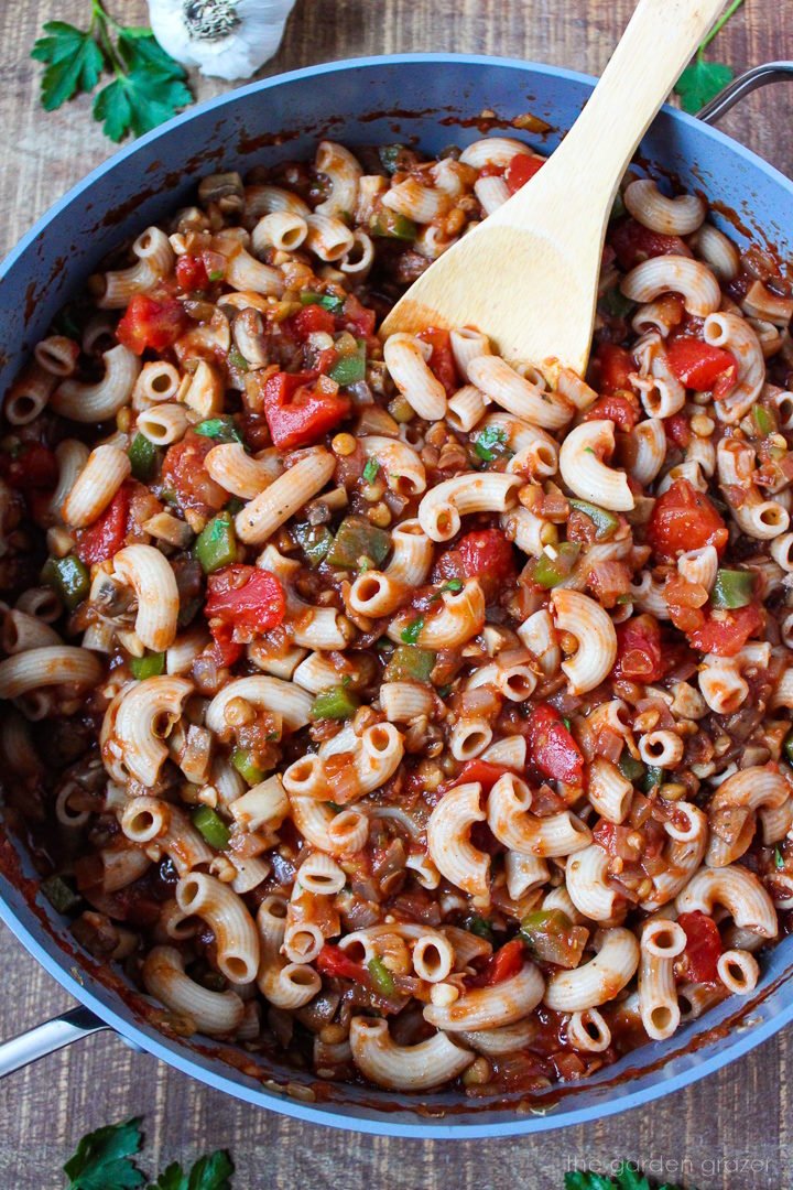 Vegan goulash with lentils and mushrooms cooking in a large skillet with wooden spoon