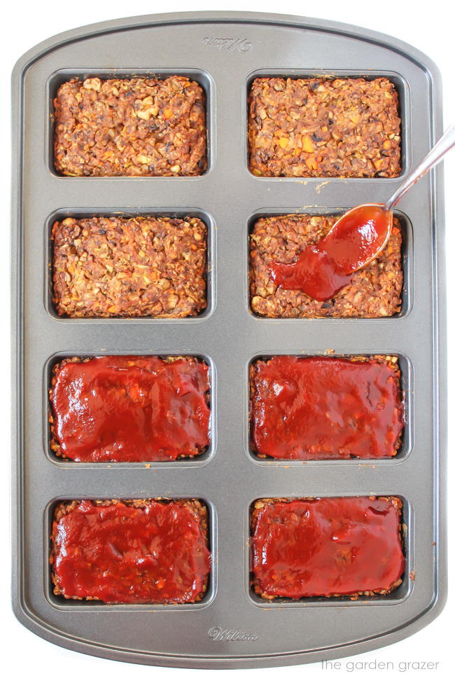 Mushroom lentil loaves in a pan being topped with tomato glaze