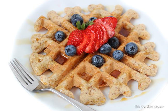 Vegan gluten-free waffle on a white plate with fresh fruit and fork