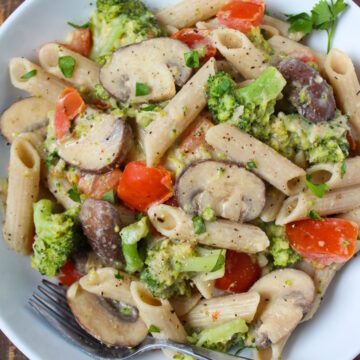 Overhead view of vegan creamy vegetable pasta served in a white bowl with fork